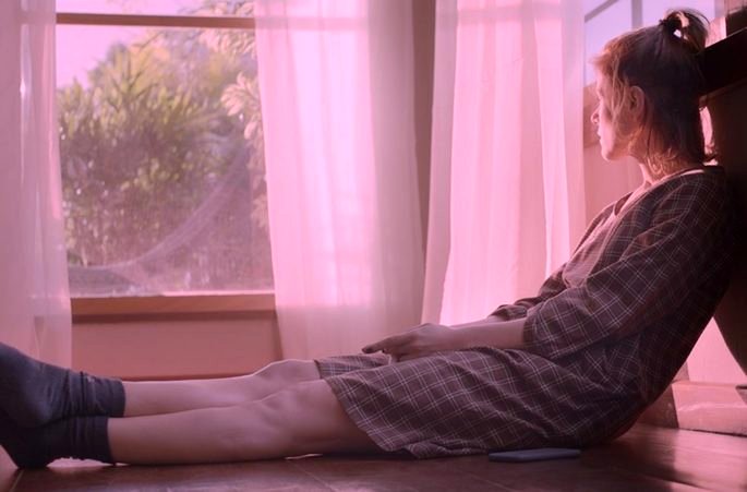 Una mujer sentada en el alféizar de una ventana mirando una enorme nube rosa
