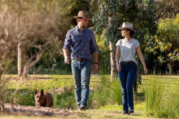 Una pareja enamorada, paseando por una granja, con un perro marrón.