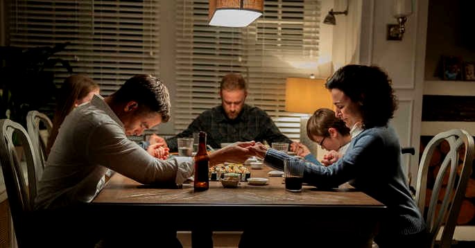 Una familia rezando alrededor de la mesa