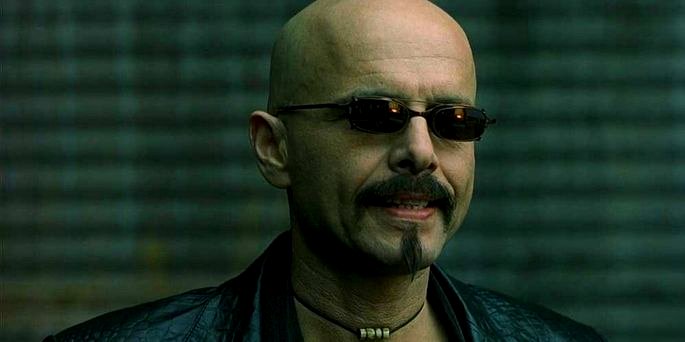Un hombre calvo con gafas de sol y un abrigo negro.