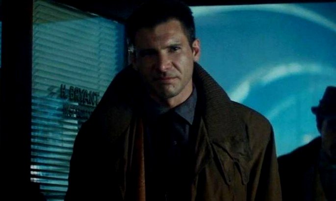 Harrison Ford interpreta a Deckard en Blade Runner. Está de pie con un abrigo marrón y una atmósfera azulada.