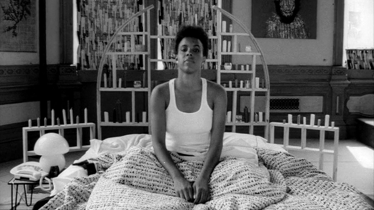Una escena de la película She Wants Everything muestra a una mujer negra sentada en una cama doble.
