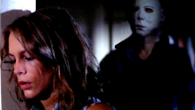 Un hombre enmascarado se acerca a una mujer joven de espaldas.