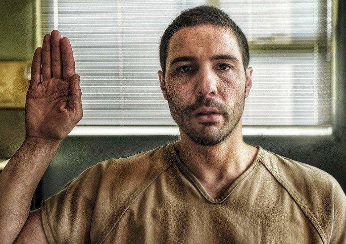 Un hombre vestido de preso levantando la mano para testificar ante la justicia