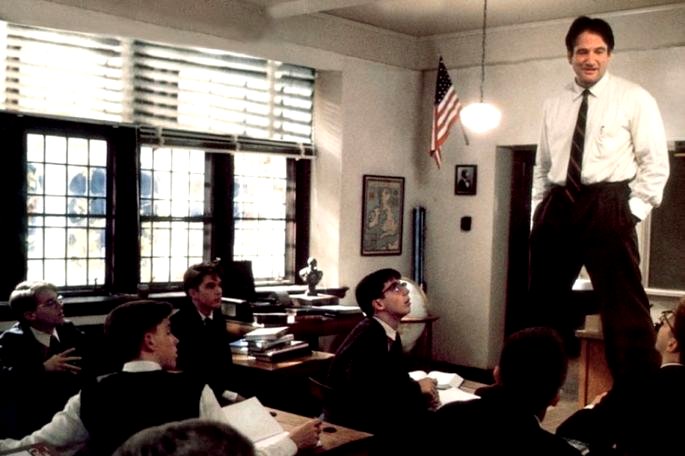 Profesor dando una clase de pie sobre la mesa.