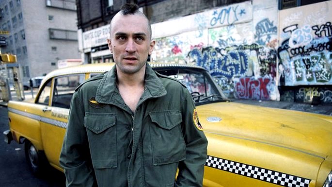 Un hombre con el pelo peinado frente a un taxi amarillo.